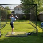 Outdoor golf practice setup with a launch monitor, hitting mat, and golf net in a backyard