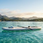 Sleek inflatable paddle board floating on clear turquoise water under bright sunlight.
