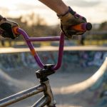 Hands gripping colorful BMX handlebars at an outdoor skatepark.