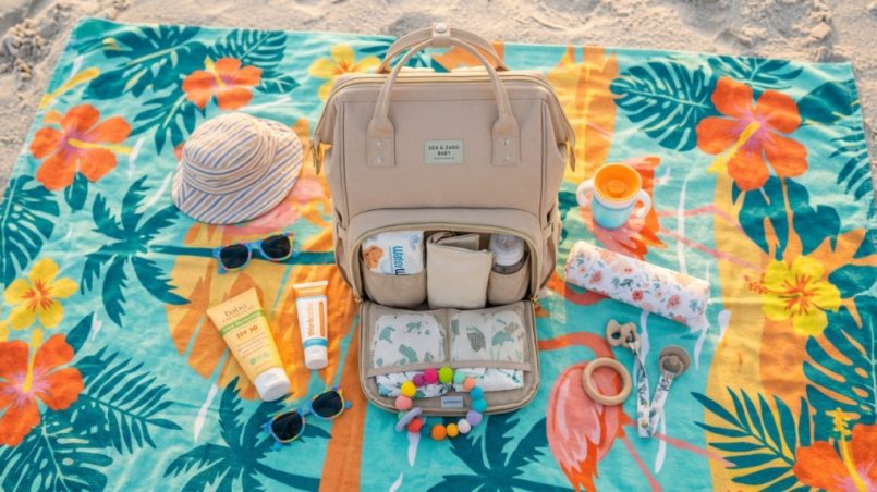 Neutral diaper bag backpack with baby essentials on sandy Florida beach.