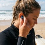 Surfer inserting a vented ear plug before surfing.