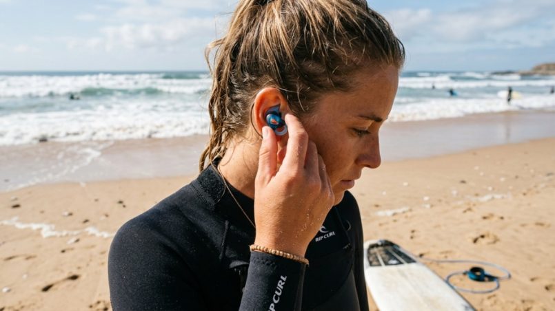 Surfer inserting a vented ear plug before surfing.