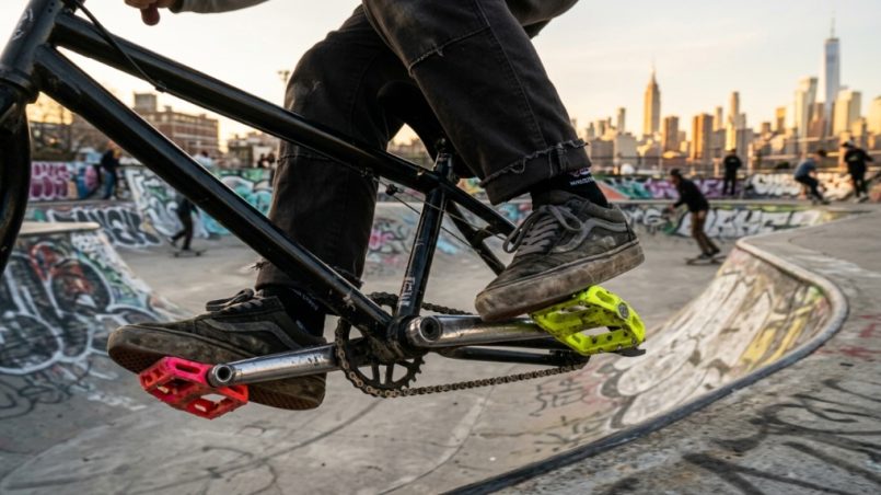 Rider performing a trick on BMX pedals at a New York skatepark.