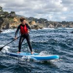 Paddleboarder gliding on calm California coastal waters during sunset.