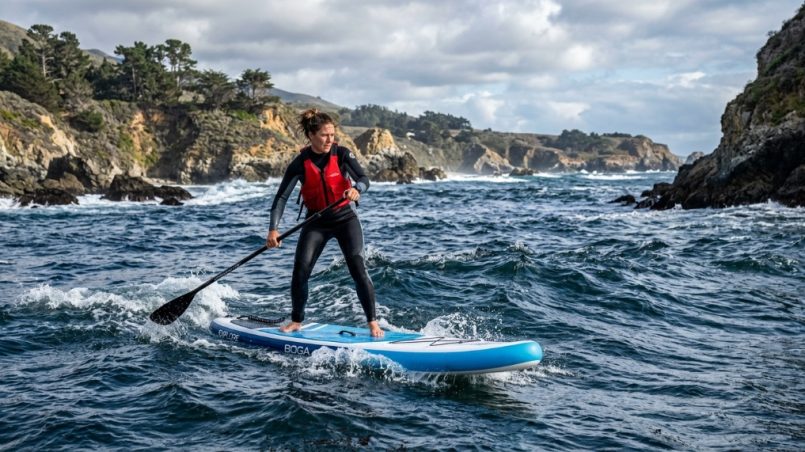 Paddleboarder gliding on calm California coastal waters during sunset.